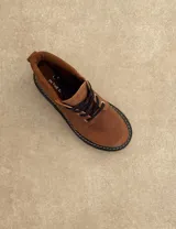 Borcego de cuero color gris con cordones color naranja, suela track negra de goma y detalle de gamuza en la parte superior del tobillo.