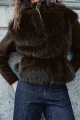 Chaqueta de punto gris con frente de piel sintética, cuello redondo, manga larga y cinturón fino efecto piel incorporado en la cintura. Cuenta con cierre frontal mediante ganchos metálicos y forro interior.