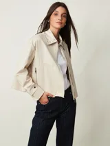 Campera cruda de gabardina con cierre frontal, bolsillos con cierre y cuello mao adornado con tachas plateadas.
