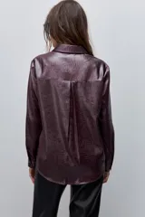 Camisa blanca de calce relajado con acabado satinado y brillo sutil, cuello clásico, cierre frontal con botones y mangas largas con puños.