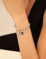 Charm circular bañado en oro, con cristal facetado en color azul zafiro.