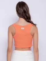 Top blanco de tela texturada, sin mangas y con cuello redondo. Cuenta con cuatro botones y terminación en curva en la parte delantera.