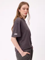 Remera de algodón con corte holgado, color crema, con estampado gráfico en la espalda que incluye un sol, montañas y mariposas con la frase Realities Rusty Collide.