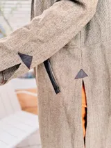 Tapado largo de paño liviano con diseño de cuadros en tonos marrones. Presenta solapas clásicas, bolsillos laterales con detalles en cuero y tajos profundos en los costados.