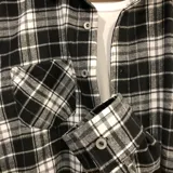 Sobrecamisa de franela a cuadros blancos, negros y grises, de manga larga, con cuello camisero, cierre abotonado y bolsillo en el pecho.