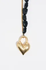 Collar de doble cadena, una de eslabones dorados y otra de piedras negras irregulares, con un dije central en forma de corazón dorado y cierre tipo T.