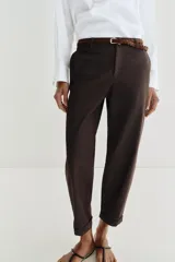 Pantalón chino de tiro bajo color marrón oscuro, con pernera recta y bajo con vuelta. Incluye un cinturón trenzado delgado de color marrón claro. Cuenta con bolsillos delanteros y cierre frontal con cremallera y botón.