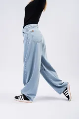 Jean de tiro alto con corte barrel leg, estilo globo, confeccionado en denim de tono azul claro. Presenta costuras reforzadas en la zona de las rodillas y un diseño de pierna ancha que se estrecha sutilmente hacia el tobillo.