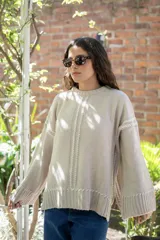 Sweater oversize de tejido de punto color beige, con cuello a la base y mangas largas acampanadas. Presenta detalles bordados a mano en color blanco en el frente, hombros y ruedo.