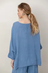 Blusa de lino color verde militar, holgada, de manga 3/4 con volados en los puños, cuello redondo y detalle de alforzas horizontales en el dobladillo.