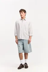 Camisa de manga larga con diseño a rayas verticales en tonos claros, cuello clásico, bolsillo delantero en el pecho y cierre frontal con botones.