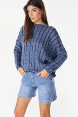 Sweater crop de tejido de punto con diseño trenzado y rayas verticales en combinación de tonos beige y tostado, cuello redondo y mangas murciélago largas. Cuenta con un parche de cuerina marrón con la marca grabada en el borde inferior.