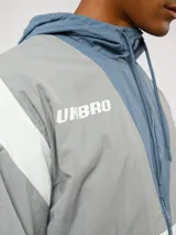 Campera de nylon Umbro con capucha, cierre frontal y diseño de bloques de color en gris, blanco y azul. Puños y dobladillo elásticos.
