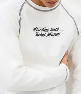 Remera de manga larga confeccionada en tejido de algodón acanalado (ribana) color blanco. Presenta costuras contrastantes en color oscuro, cuello redondo y estampa frontal con lettering en estilo gótico.