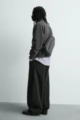 Bandolera negra de formato vertical con textura, diseño geométrico y correa ajustable para llevar al hombro.