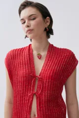 Kimono tejido de punto en color crudo con sutil brillo de lurex. Presenta un diseño sin mangas, corte largo y cierre frontal mediante dos lazos finos. El tejido tiene una textura acanalada vertical.