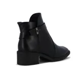 Bota de cuero negra de caña baja, con taco cuadrado y punta fina. Presenta una correa con hebilla alrededor del tobillo y un aplique metálico en el lateral. Cuenta con cierre lateral.