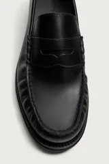 Mocasín de vestir color marrón oscuro, fabricado en cuero, con detalle de antifaz en el empeine y suela a tono con ligero tacón.