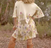 Vestido corto acampanado color crudo, con estampado artesanal de hojas en tonos marrones, violetas y amarillos. Tiene cuello redondo y mangas cortas amplias.