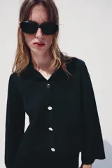 Chaqueta de punto color azul marino, con cuello solapa, manga larga y cierre frontal con botones metálicos. Presenta terminaciones en ondas en el bajo y los puños.