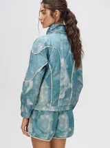 Short de estilo deportivo con pretina elástica, confeccionado en tela satinada con estampado tipo tie-dye en tonos azul y blanco. Presenta bordes con vivo en color crema y un pequeño logo bordado en la parte inferior.