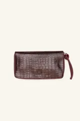 Billetera rectangular de cuero con textura de reptil, cierre perimetral y correa de muñeca lateral. Presenta un pequeño aplique metálico circular en el centro.