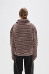Buzo de textura afelpada con diseño de rayas horizontales finas en tonos marrones. Presenta cuello alto con cierre frontal parcial y mangas largas holgadas.