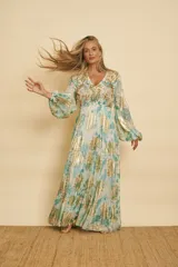 Vestido largo con estampado floral en tonos verde y blanco, con detalles metálicos dorados brillante, escote en V, mangas largas abullonadas y falda de paneles fruncidos.