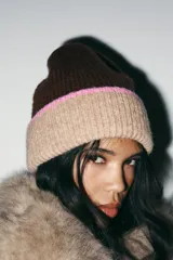 Gorro tipo beanie de punto, con diseño bicolor que combina marrón oscuro en la parte superior y beige en el borde, con una franja delgada en color rosado que separa ambos tonos.