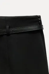 Pantalón culotte negro de tiro medio con trabillas y cinturón fino efecto piel con hebilla metálica. Presenta raya planchada y cierre de cremallera oculta en la costura.