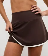 Short pollera deportivo de microfibra, color marrón con borde inferior contrastante en color blanco. Presenta un diseño ajustado y funcional, ideal para actividades físicas.