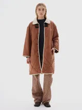 Tapado largo hasta las rodillas, color marrón, con vivos en color crema y cuello de pana. Tiene bolsillos delanteros, cierre frontal con botones a presión y cordón en la cintura para ajustar.