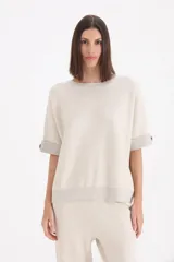 Sweater de punto color beige, con cuello redondo, mangas cortas con dobladillo y detalle de botón lateral, y terminaciones en lurex.