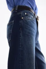 Jean de tiro alto y diseño barrel en denim de algodón azul, con corte de cinco bolsillos, cierre frontal con botón y cremallera, y piernas de corte curvo y holgado.