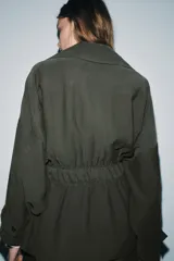 Trench corto de Zara, confeccionado en mezcla de lyocell, color verde militar. Presenta cuello solapa, manga larga con hombro caído y puños con trabilla. Incluye bolsillos delanteros de plastrón, cierre frontal cruzado con botón y cinturón de lazada en el mismo tejido.
