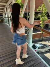 Short de denim azul con efecto desgastado, tiro medio y botamanga con flecos deshilachados.
