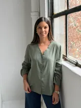Blusa de color verde oliva con escote en V, cierre frontal con botones y mangas largas con puños elásticos.