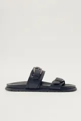 Sandalias planas de cuero negro con diseño de dos tiras ajustables con hebillas metálicas.
