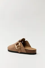 Zueco de estilo casual con capellada cerrada en material tipo gamuza color negro. Presenta una hebilla metálica decorativa en tono dorado sobre el empeine y una base anatómica con efecto corcho.