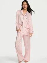 Pijama de satén de corte relajado, con diseño a rayas rosadas y blancas, compuesto por una camisa de manga larga con botones frontales, cuello con solapa, bolsillos y ribetes oscuros, y un pantalón largo a juego.