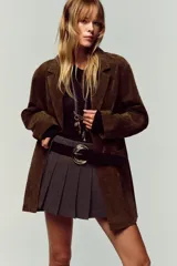 Falda pantalón gris de tiro medio con pliegues delanteros y cinturón ancho negro con hebilla plateada. Cierre lateral con cremallera oculta.