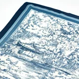 Pañuelo de forma triangular con estampado estilo toile de jouy en tonos azul y blanco, con bordes definidos en azul oscuro.
