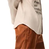 Camisa de manga larga Lacoste en color beige, con cuello abotonado y cierre frontal de botones. Presenta un estampado gráfico grande en el frente con el nombre de la marca, el logo del cocodrilo y la leyenda 'French Sportswear est. nineteen thirty three'. Incluye un pequeño logo bordado en el puño de la manga izquierda.