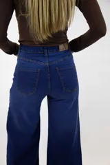 Pantalón jean de tiro alto y corte campana en color azul medio, con bolsillos delanteros y traseros, y cierre frontal con botón y cremallera.