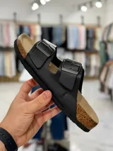 Sandalias de dos tiras negras con hebillas metálicas ajustables, plantilla anatómica y suela plana.