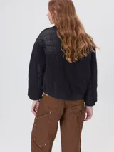 Campera crop de corte boxy y color negro, forrada en corderito, con parches capitoneados en el pecho y las mangas. Cuenta con cierre frontal metálico, cuello alto, puños y bajo elastizados, y detalle de logo bordado en hilo en el pecho.