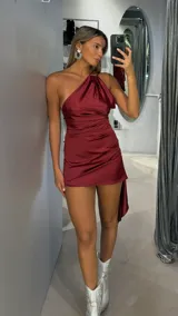 Vestido corto de satén color bordó, con diseño de un solo hombro y drapeado lateral. Presenta un corte asimétrico en el ruedo con una caída más larga en uno de los laterales.