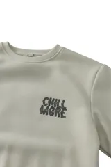 Buzo de felpa color beige con cuello redondo, mangas largas y estampa grande en la espalda con la frase "Chill More" en tonos grises.