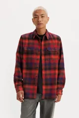 Camisa de franela a cuadros rojos, negros y azules, de corte recto, manga larga, con cuello clásico, cierre frontal con botones, dos bolsillos con solapa abotonada en el pecho y puños abotonados.