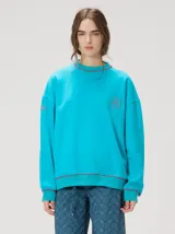 Buzo oversize turquesa con cuello redondo, puños ajustados y detalles de costuras y bordados en rojo.